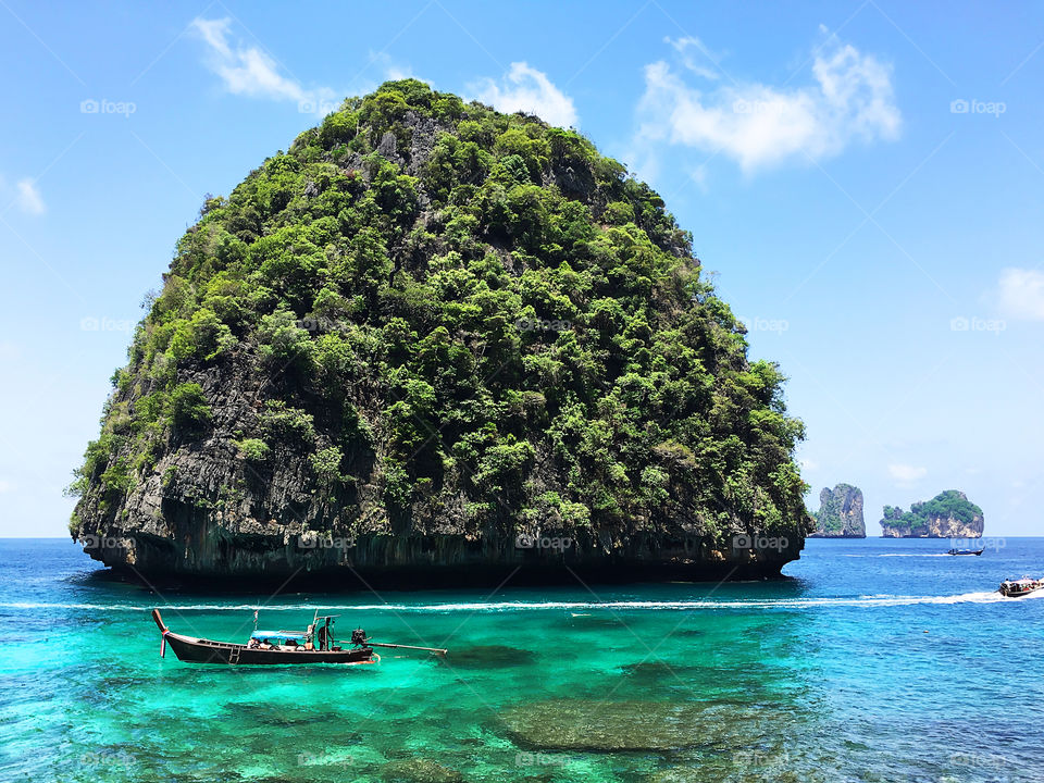 Boat standing in front of a green tropical island in turquoise sea water in Thailand 