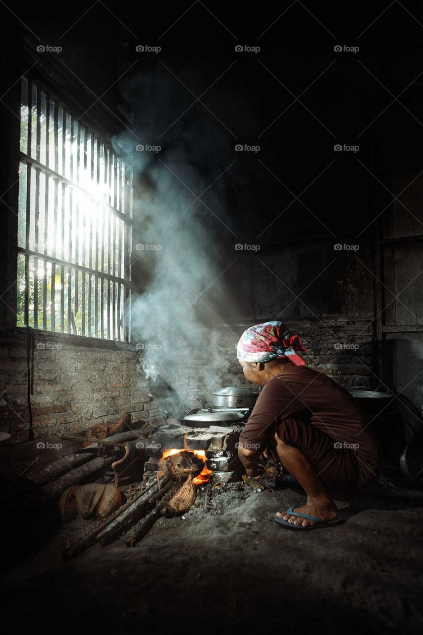 The smoke is getting out from the window slits- July 1, 2018 a traditional kitchen and the woman cooking with wood fire