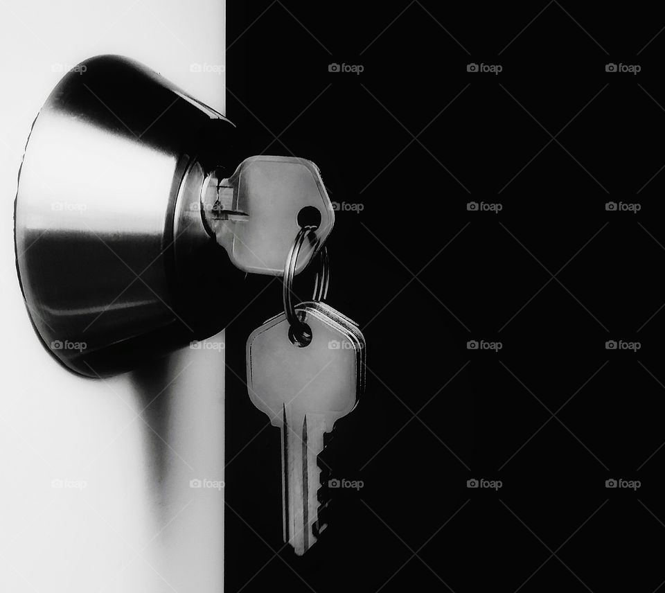 Keys hanging in a lock of a white door opening to a void of black in black and white