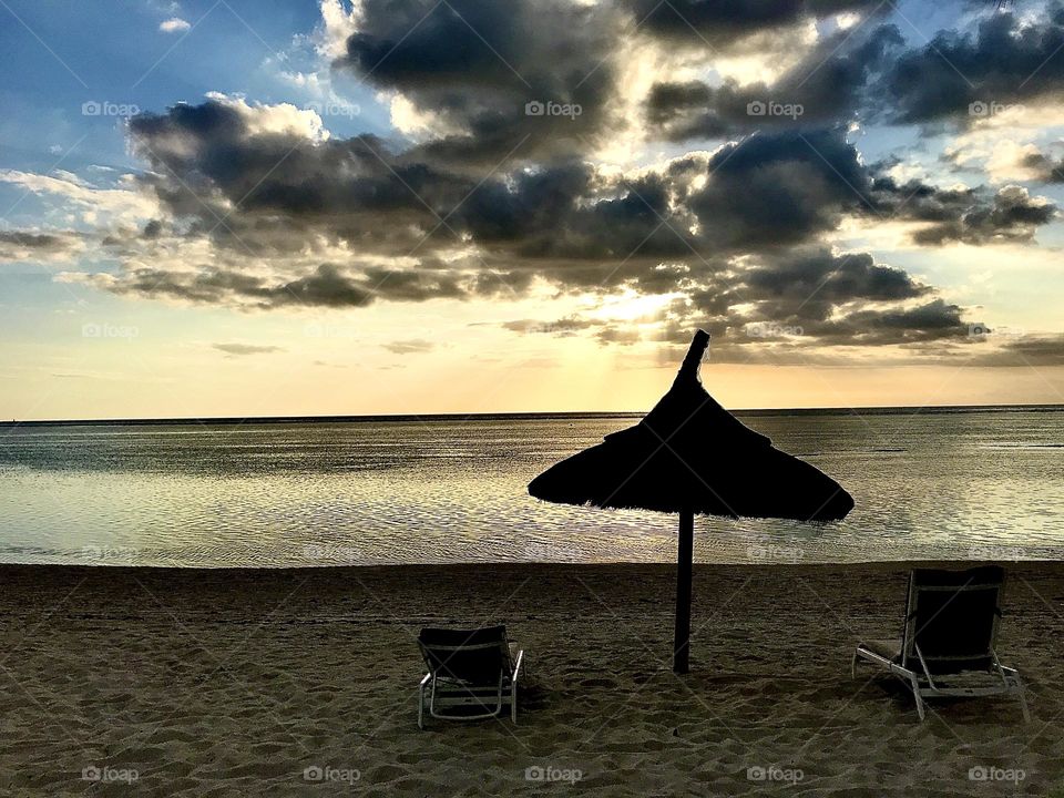 Dramatic cloudy sunset over the empty serene beach in Mauritius. Calm seas and crystal waters. Golden sky