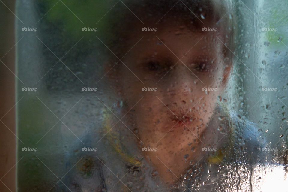sad portrait of a boy through wed glass