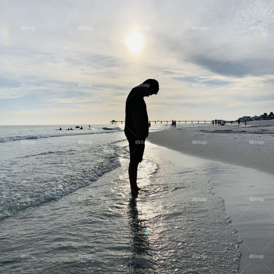 Silhouette boy standing in ocean water on sand beach sunset shore seashore 