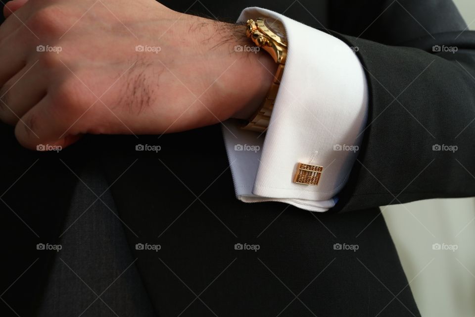 Luxury golden cufflinks. Man in tux shows golden abacus shaped cufflinks and watch
