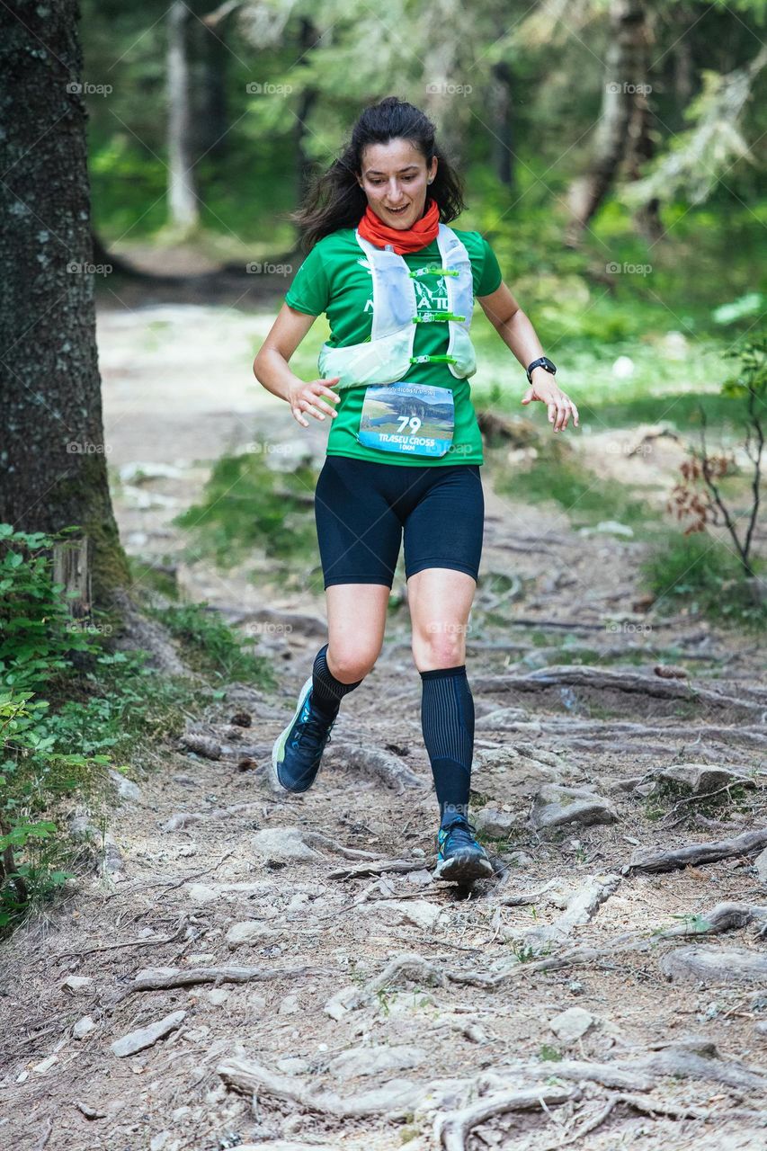 Millennial woman dressed in a green t-shirt and black shorts, running at a trail run competition.