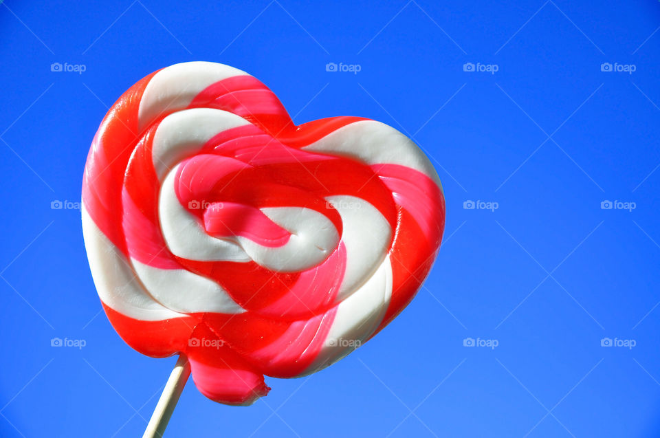 A yummy huge heart lollipop against a bright blue sky. 