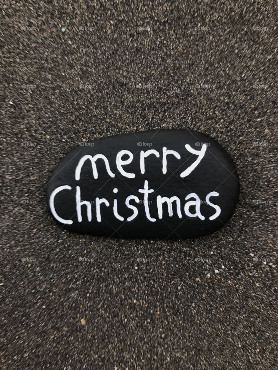 Merry Christmas on a black stone over volcanic black sand 