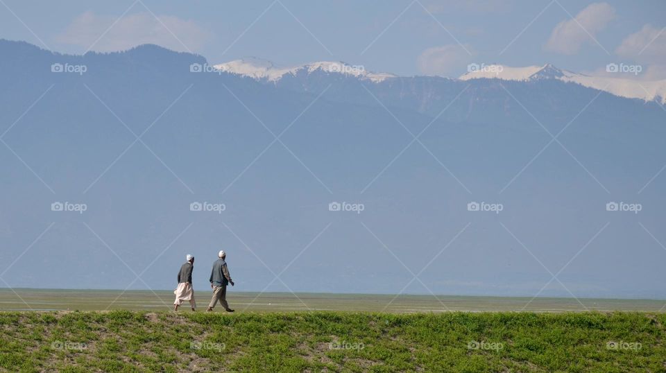 Elderly Persons Walk With Snow-covered Peaks In Backdrop