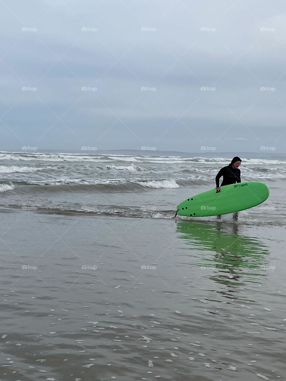 A person walking in the water with a green surf board