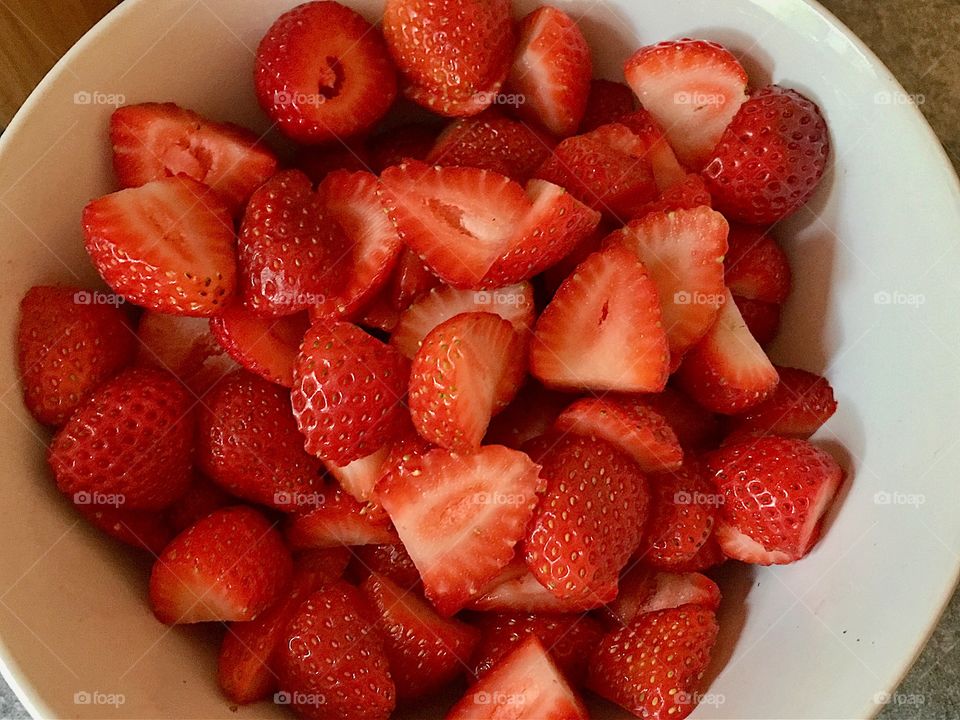 Slices fresh red strawberries in white bowl