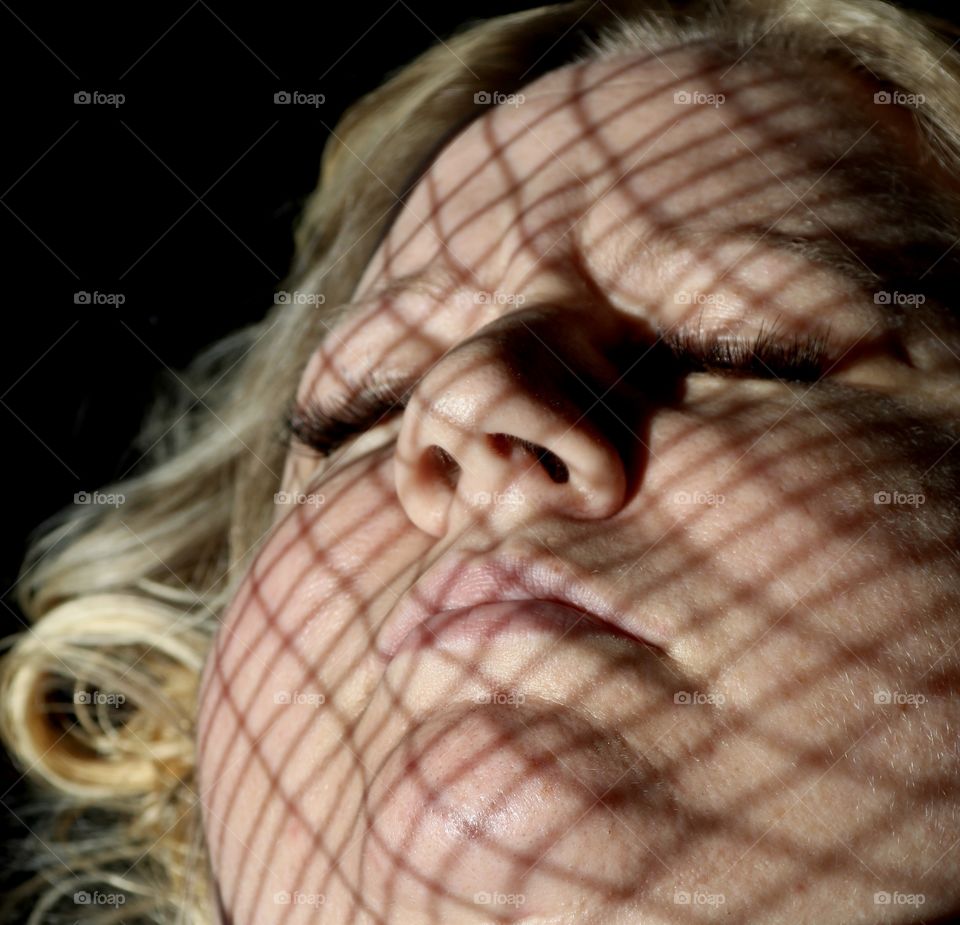 Blonde woman with shadow of tennis racket across her face 