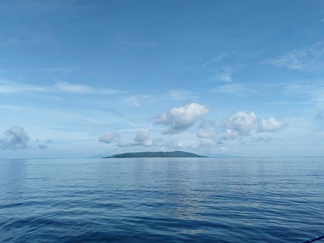 Island in the stream underneath the baby blue skies and clouds with relaxing calm sea.