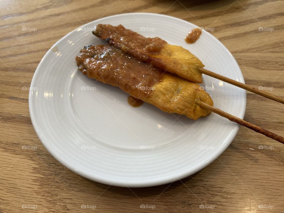 Chicken satay on a stick with brown peanut sauce on a white plate