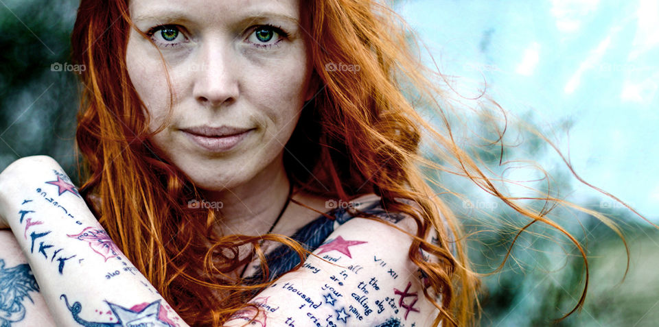 a Portrait from a woman with redhair and many tattoos in the nature 