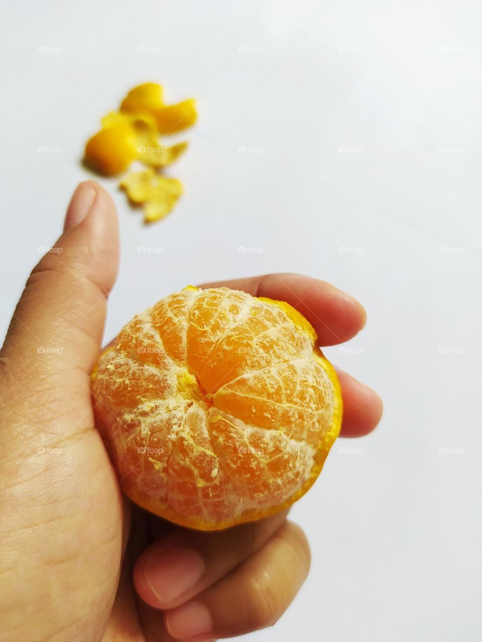Holding a ripe yellow orange that has been peeled