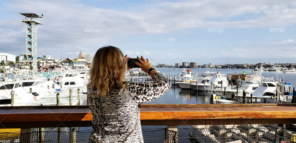 woman snapping photos of ships in harbor.