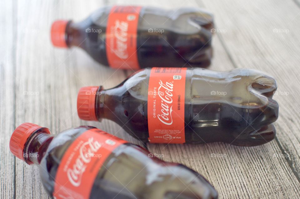 Three plastic bottles of Coca-Cola on a white rustic background