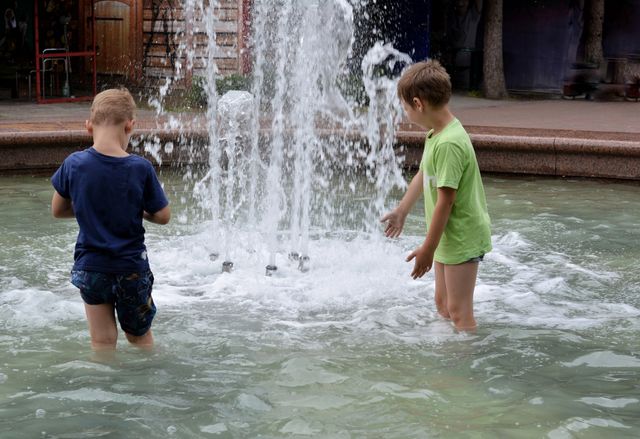 children boys in the water splash fountain, summer heat, city street view