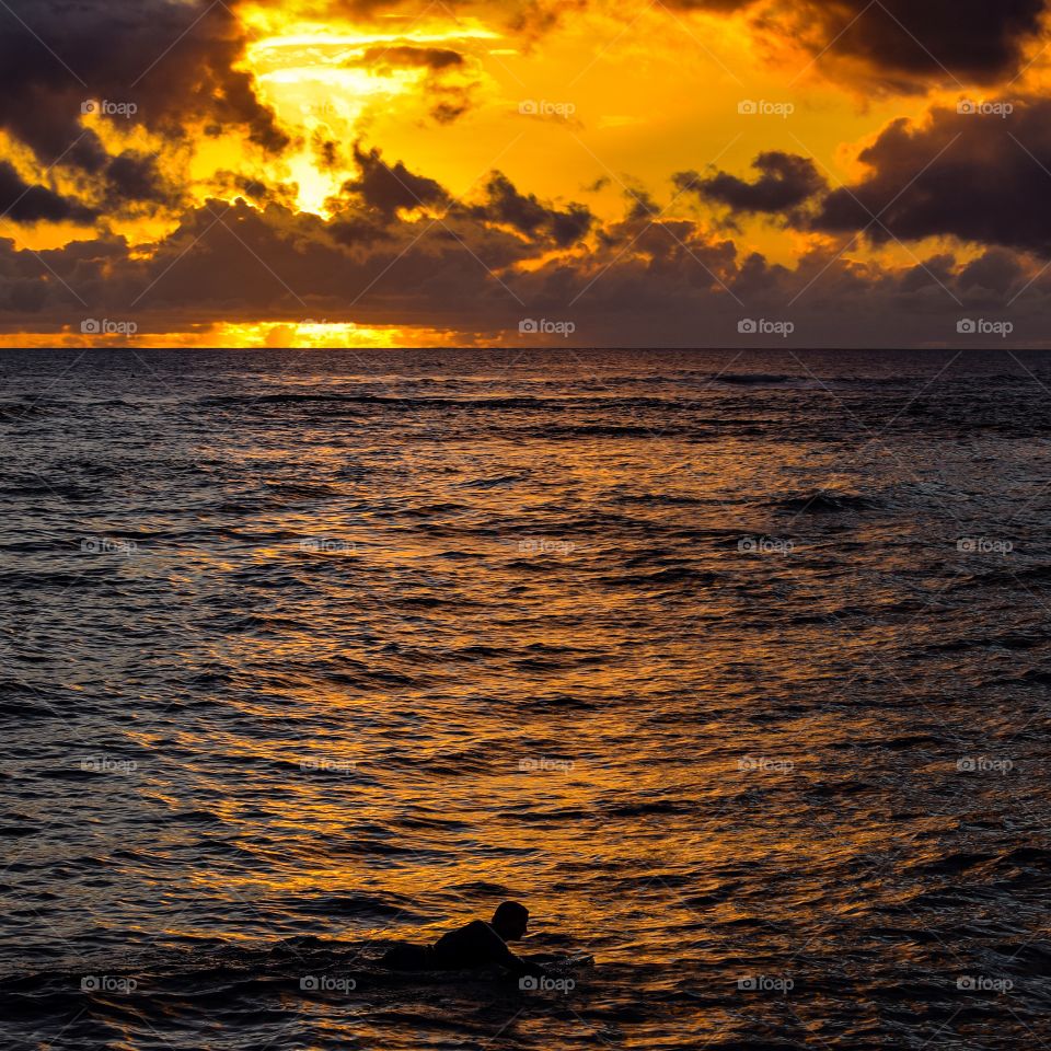 Silhouette of a surfer surfing on sea at sunset