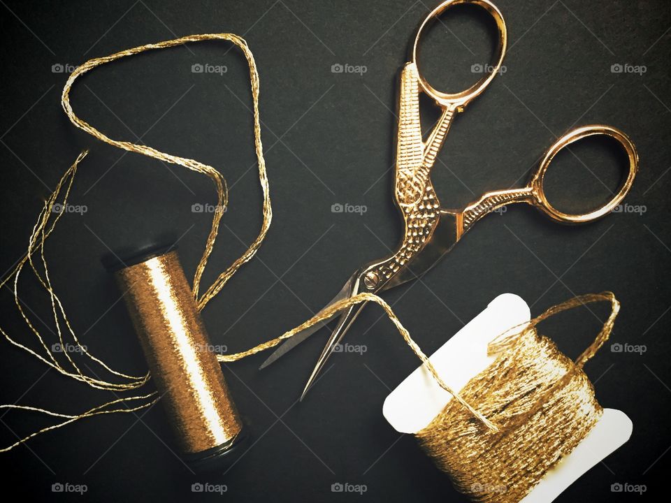 Flat lay of gold embroidery and specialty threads and golden bird needlework scissors on a black background