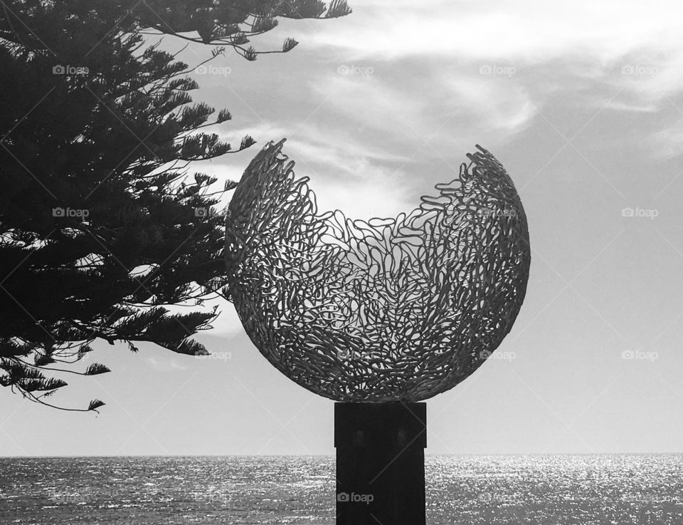 Steely grey globe against ocean backdrop, artistic monument