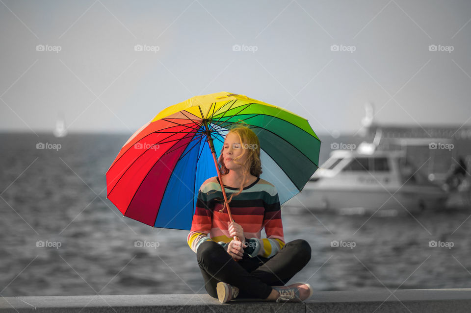 Beautiful young girl sits under a multi-colored umbrella on a warm autumn day
