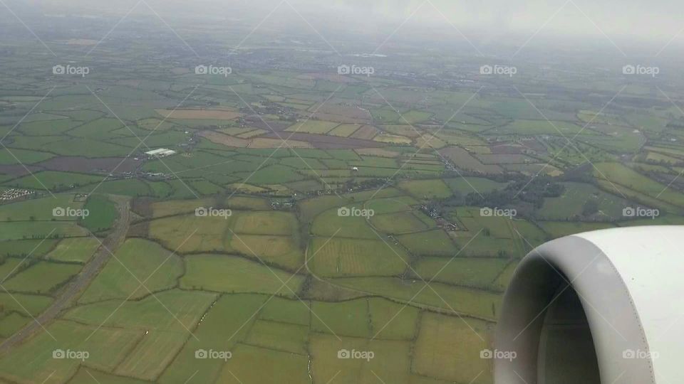 Airplane Window view flying Over Ireland, scenery of green grassy fields and farms