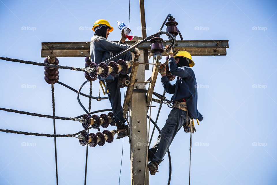 Electrician resting while working on the electricity pole to replace the electrical insulator