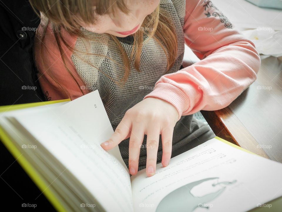 Girl seen from above is reading a book which she holds in her hands 