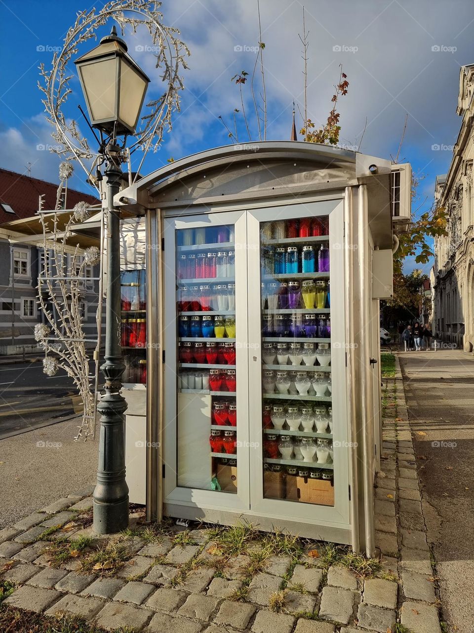 Kiosk with candles in various bright colors, next to traditional street pole
