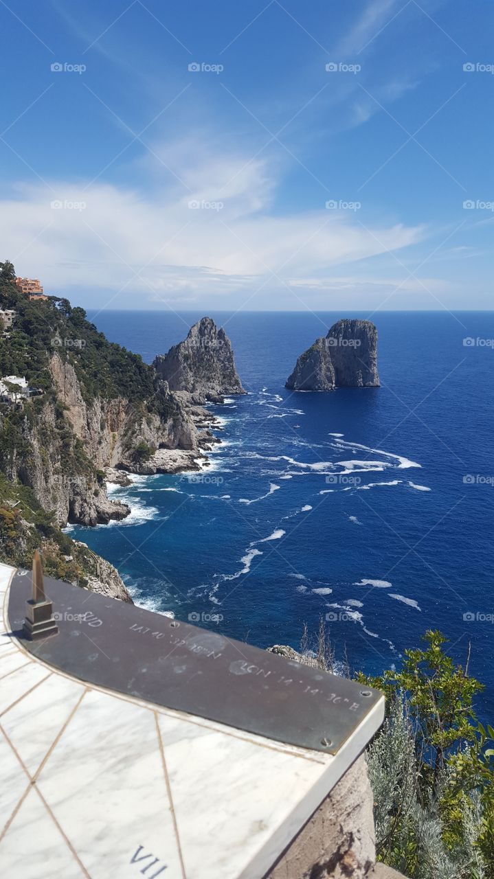 Beautiful Italian coast in the summer with cliffs, rocks and deep blue sea. Sundial in foreground.