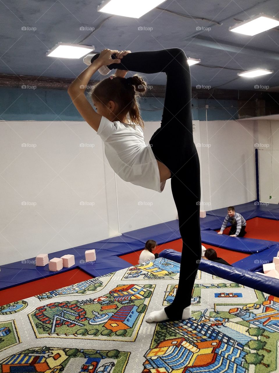 young gymnast learns a gymnastic element. While other children play, the gymnast girl continues to train hard and learns to make a ring position