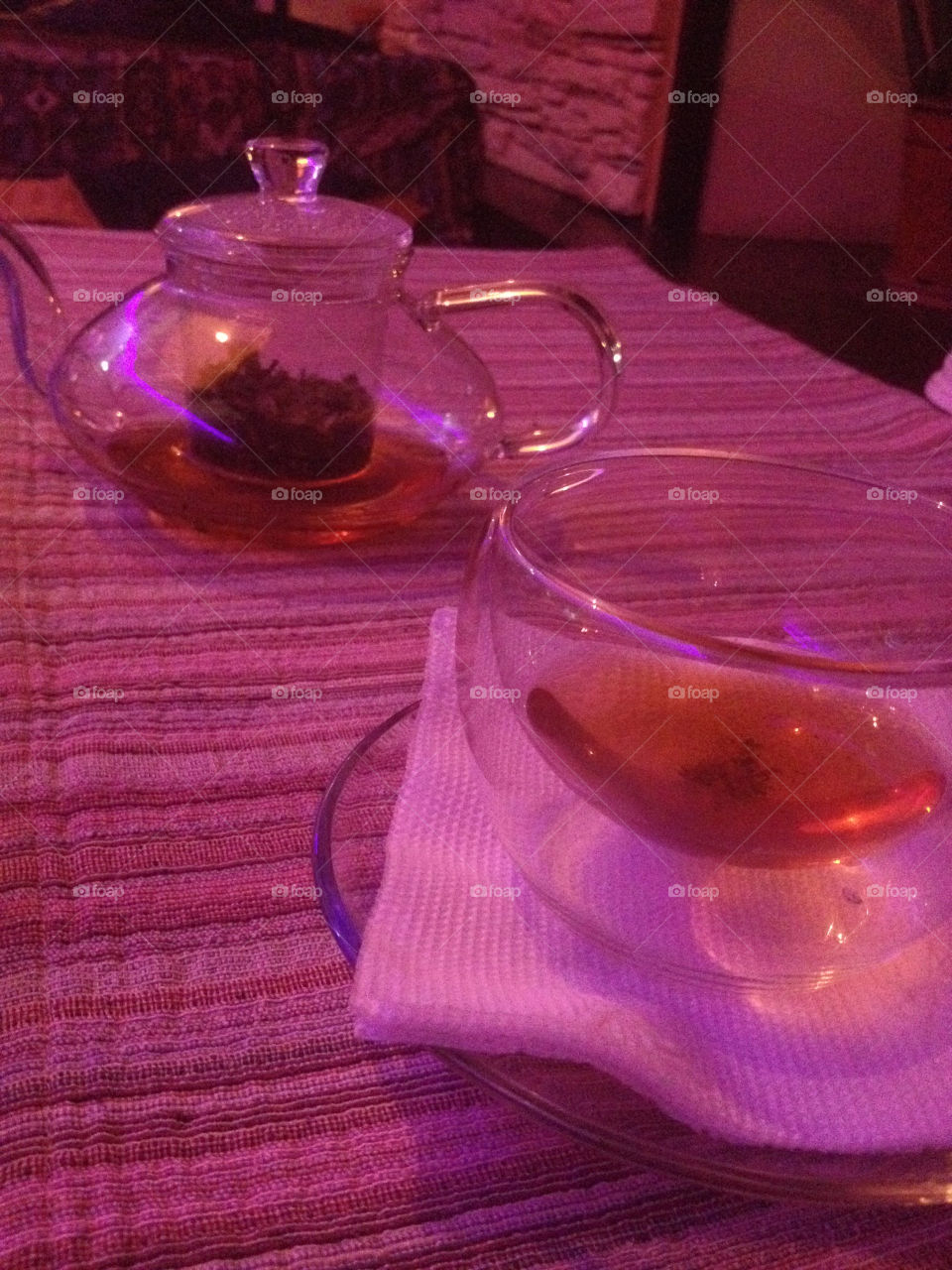 Glass Tea cup and teapot on a red tablecloth in the evening 