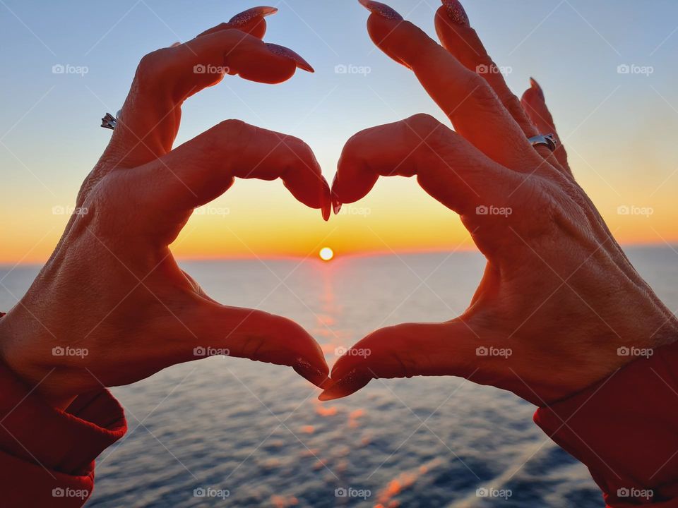female hands form a heart that frames a beautiful sunset over the sea