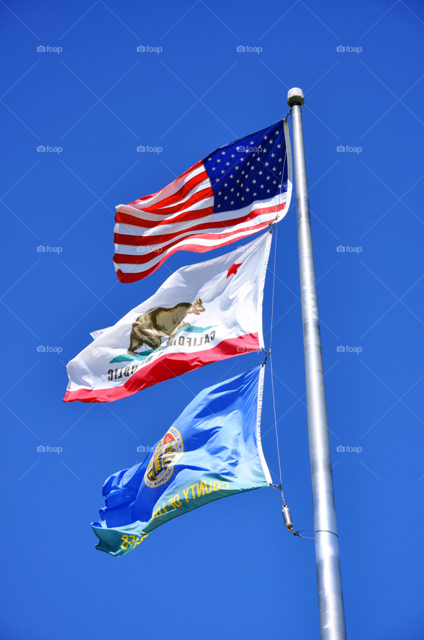 United States flag, state of California flag and Los Angles County Parks and Recreation flag blowing in the wind. 