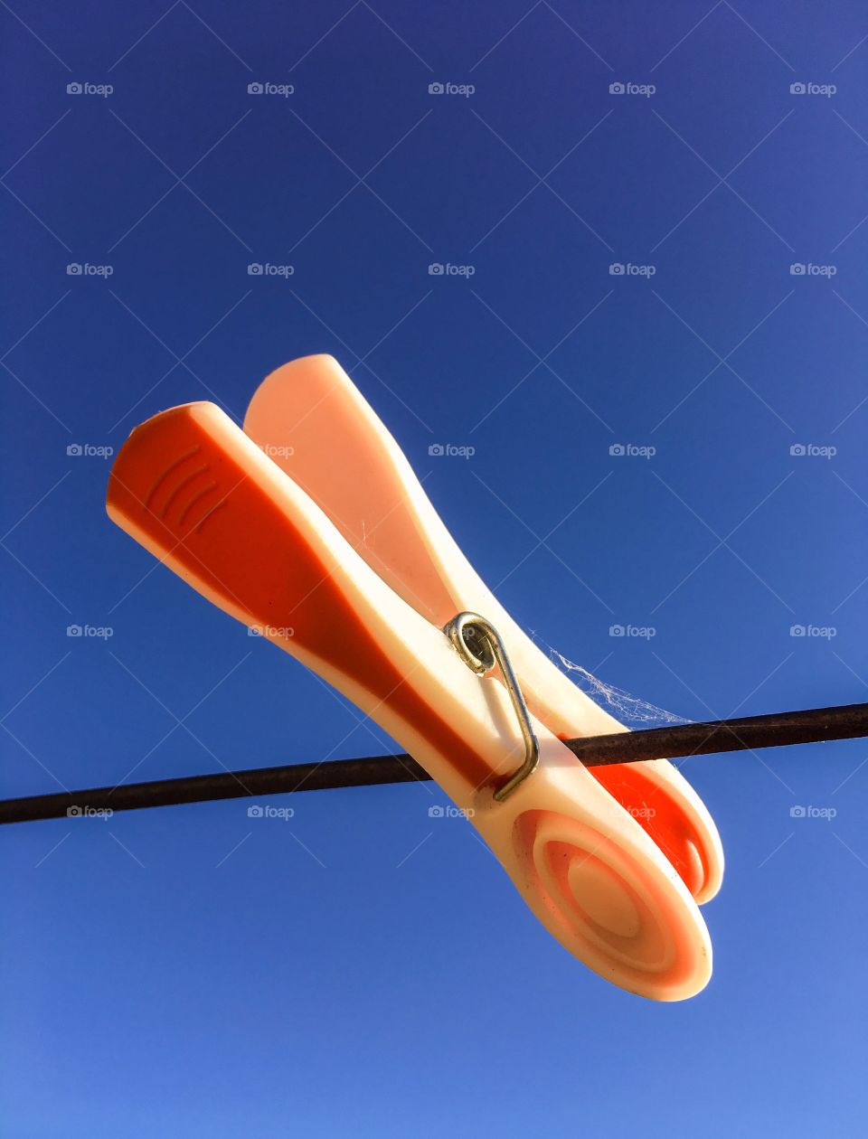 Weathered orange plastic clothespin clothes peg on a rusted wire clothesline against a vivid blue indigo sky conceptual minimalistic space for text copy