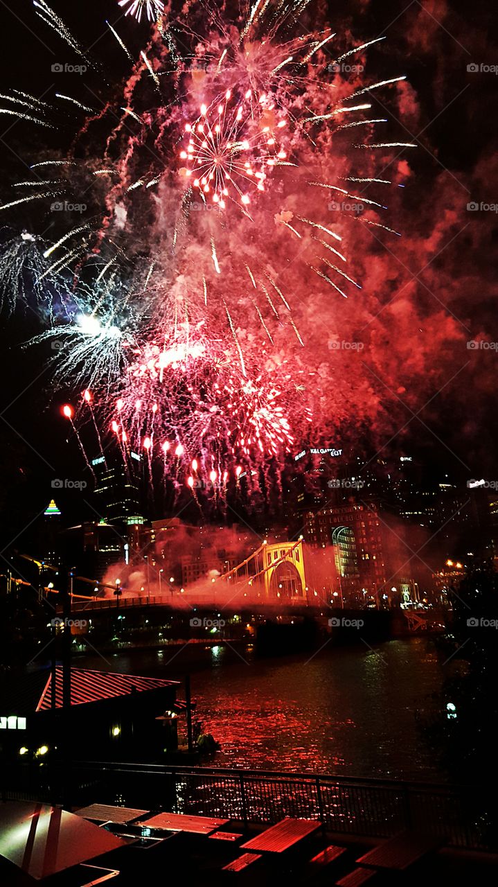 Colorful city fireworks reflecting on the river below.