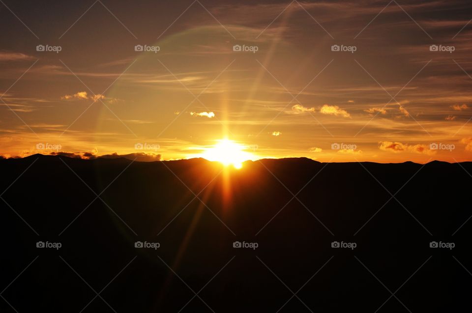 The sun rising over the silhouette of a mountain chain