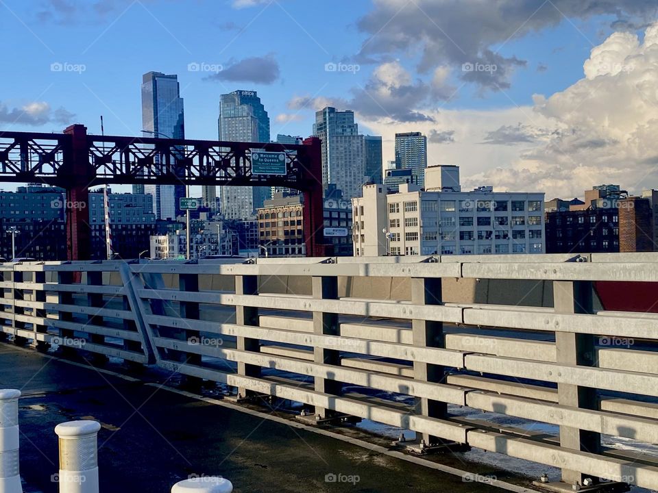 In “New York City” life goes on as usual. This is a view of the “Pulaski Bridge” against a backdrop of “Long Island City”, Queens made especially dramatic by the golden light of the setting sun. 2023. Hypnotic Productions