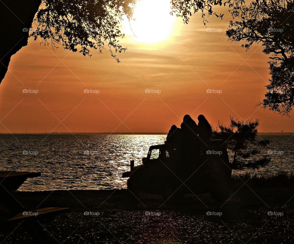 Sunset watchers - A silhouette of girls sitting on a jeep by the shore during a golden hours sunset 