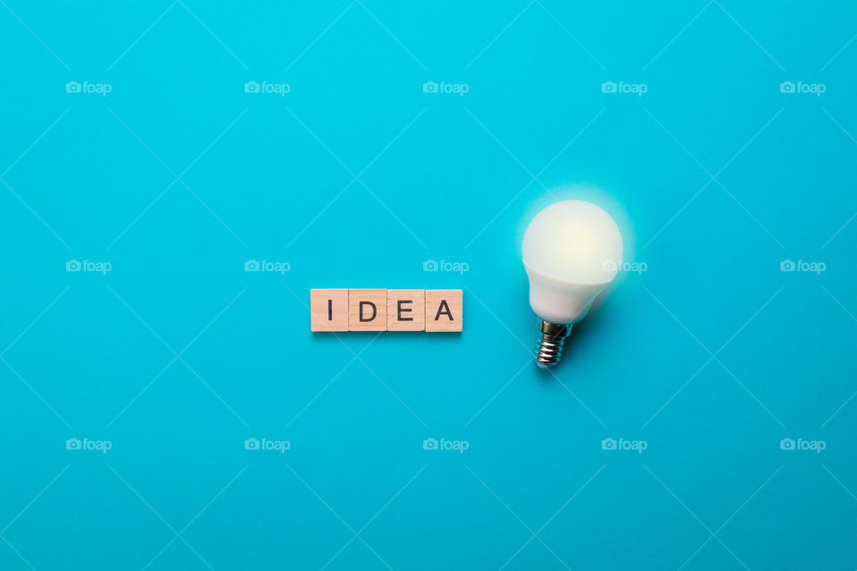 Word Idea formed from wooden letters with illuminated light bulb on blue background. Idea concept. Top view