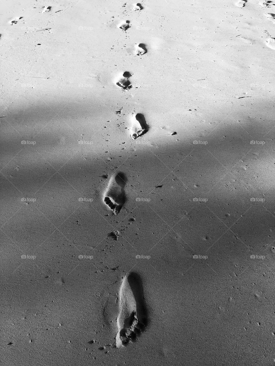 Shadow over footsteps on a sandy beach 