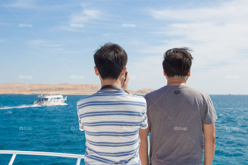 Two tourists watching the sea and capturing photos with their mobile phones.