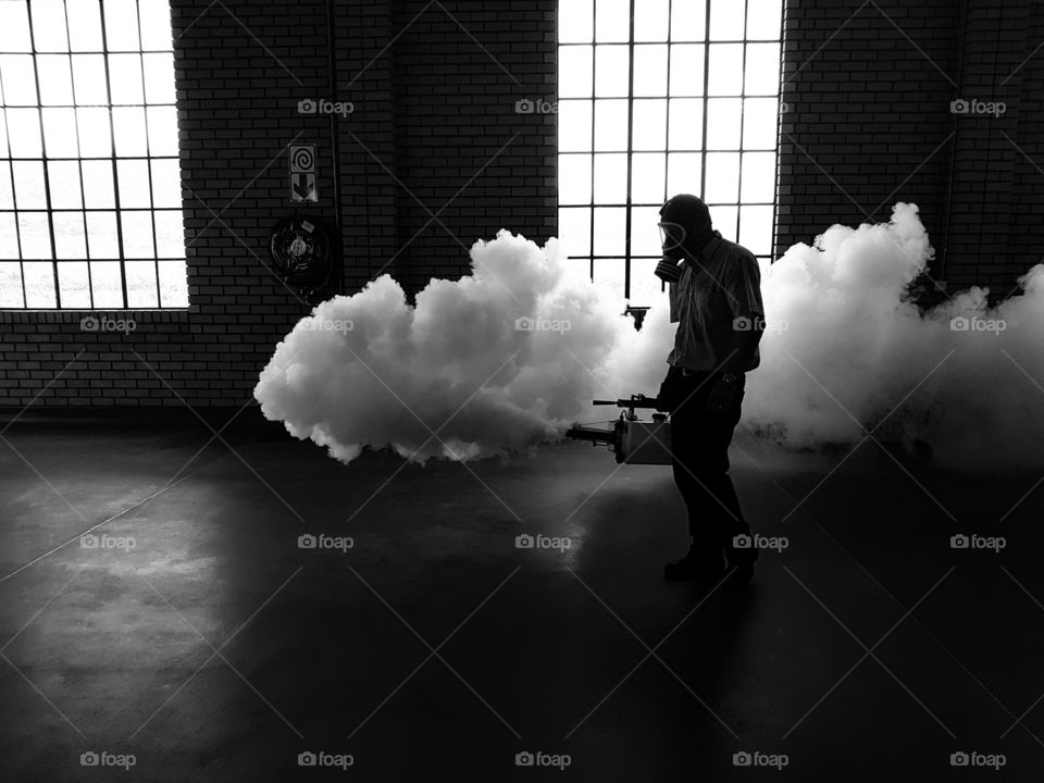 man blowing thick white smoke in a building with a fogging machine.
