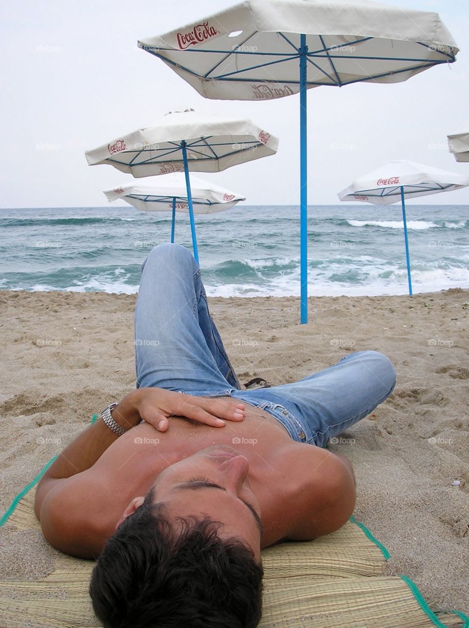 Man in jeans relaxing on the beach with parasols