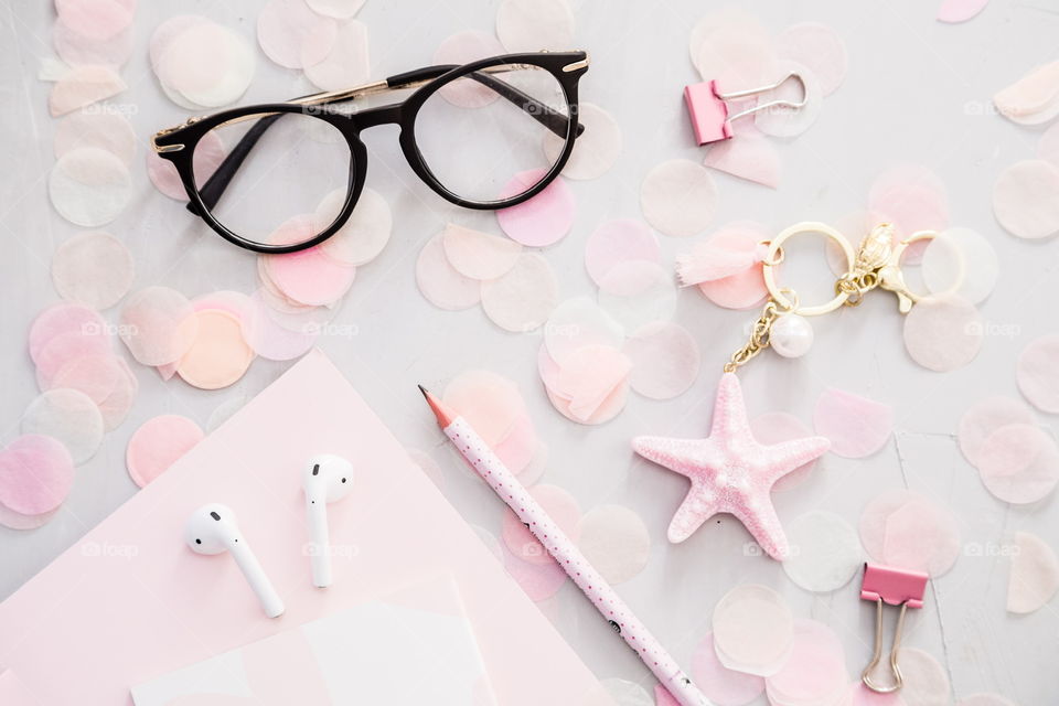 Flatlay items: reading glasses, wireless headphones, notebook, pencil, star pink color, confetti lying on gray concrete background 