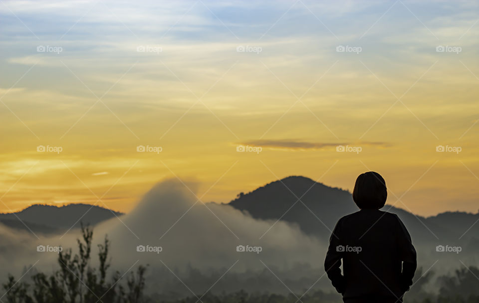 Blurry morning sun light behind the mountains with the shadow of a woman and The mist.