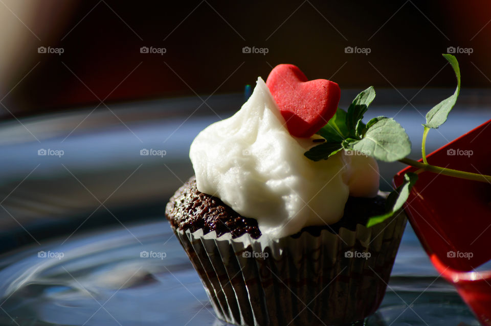 Dreamlike chocolate cupcake with red candy heart on vanilla buttercream and mint leaf arrow shining in golden hour sunlight beautiful artisanal food photography background 
