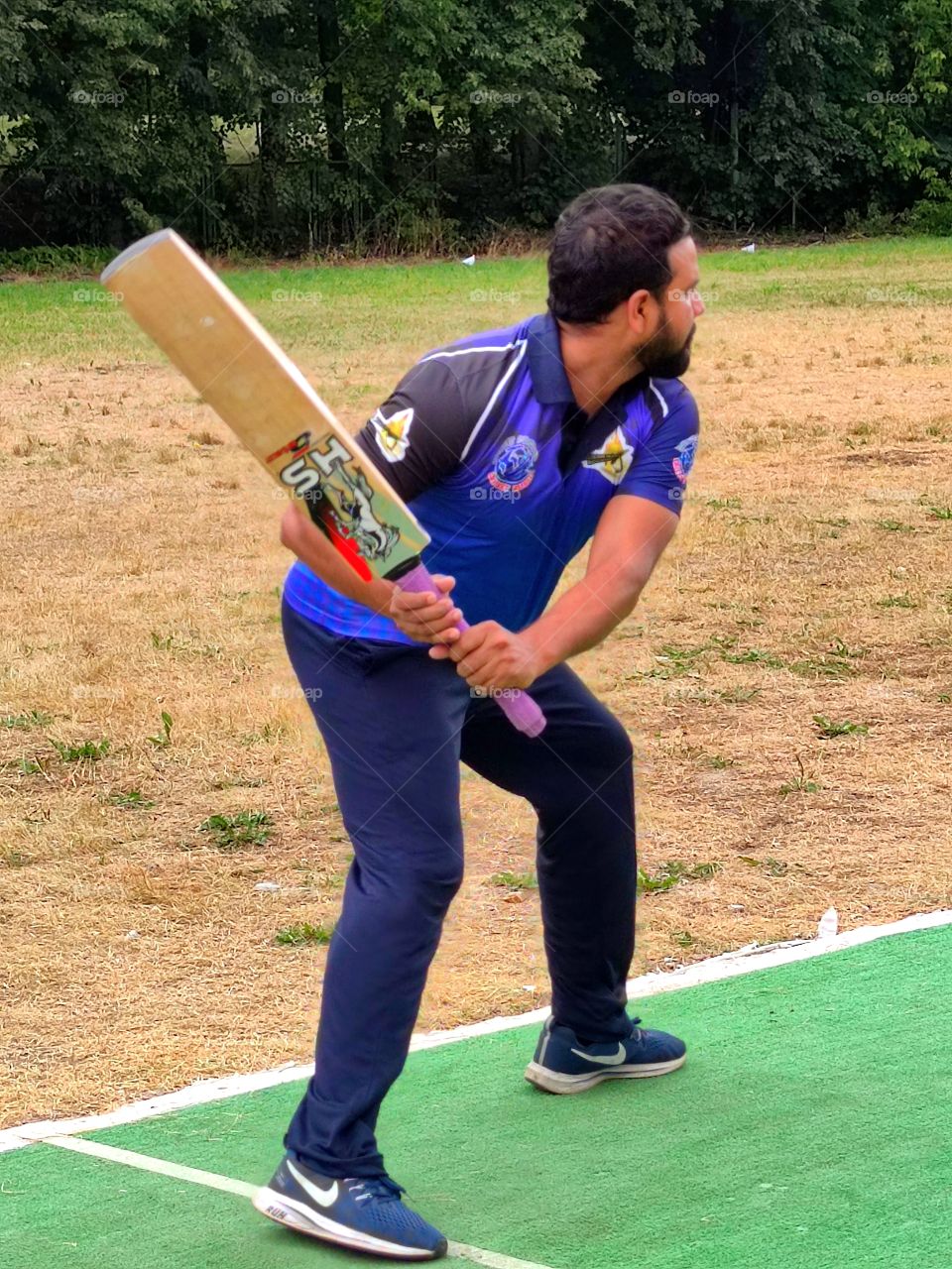 Cricket training.  A player in a blue uniform stands with a bat ready to deflect the ball