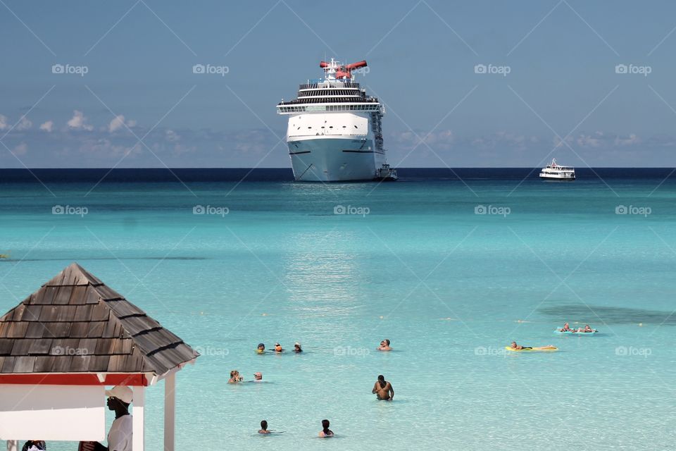 View of people in the water at a tropical beach location with cruise ship in the background