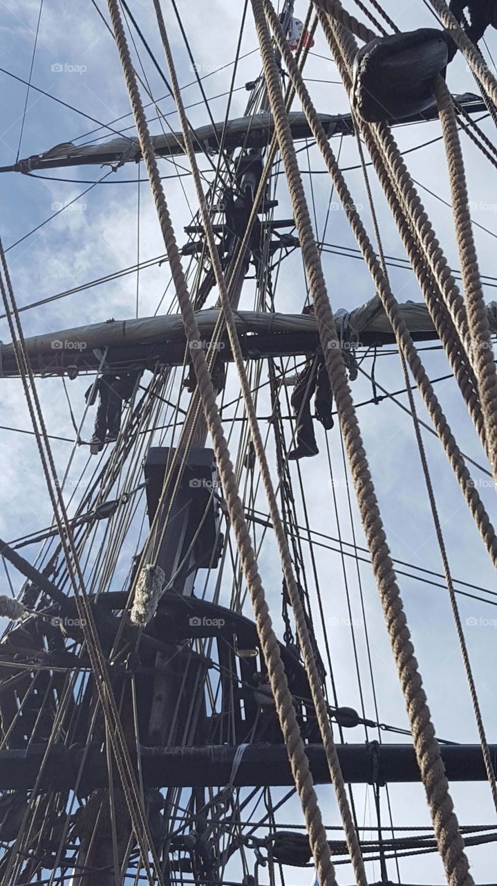 up high on a tall sailing ship's mast are a couple of people unfurling the sails in Monterey, Ca